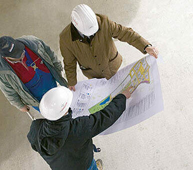 Drei Personen sehen sich gemeinsam einen Bauplan an.