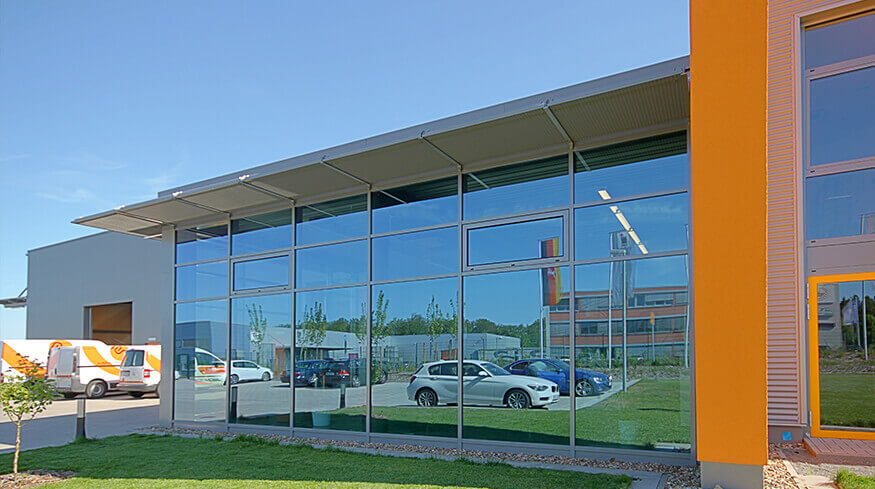 Außenansicht mit Glasfront des Eingangsbereichs des neuen Büro- und Betriebsgebäudes der ASM Dimatvec Deutschland GmbH.